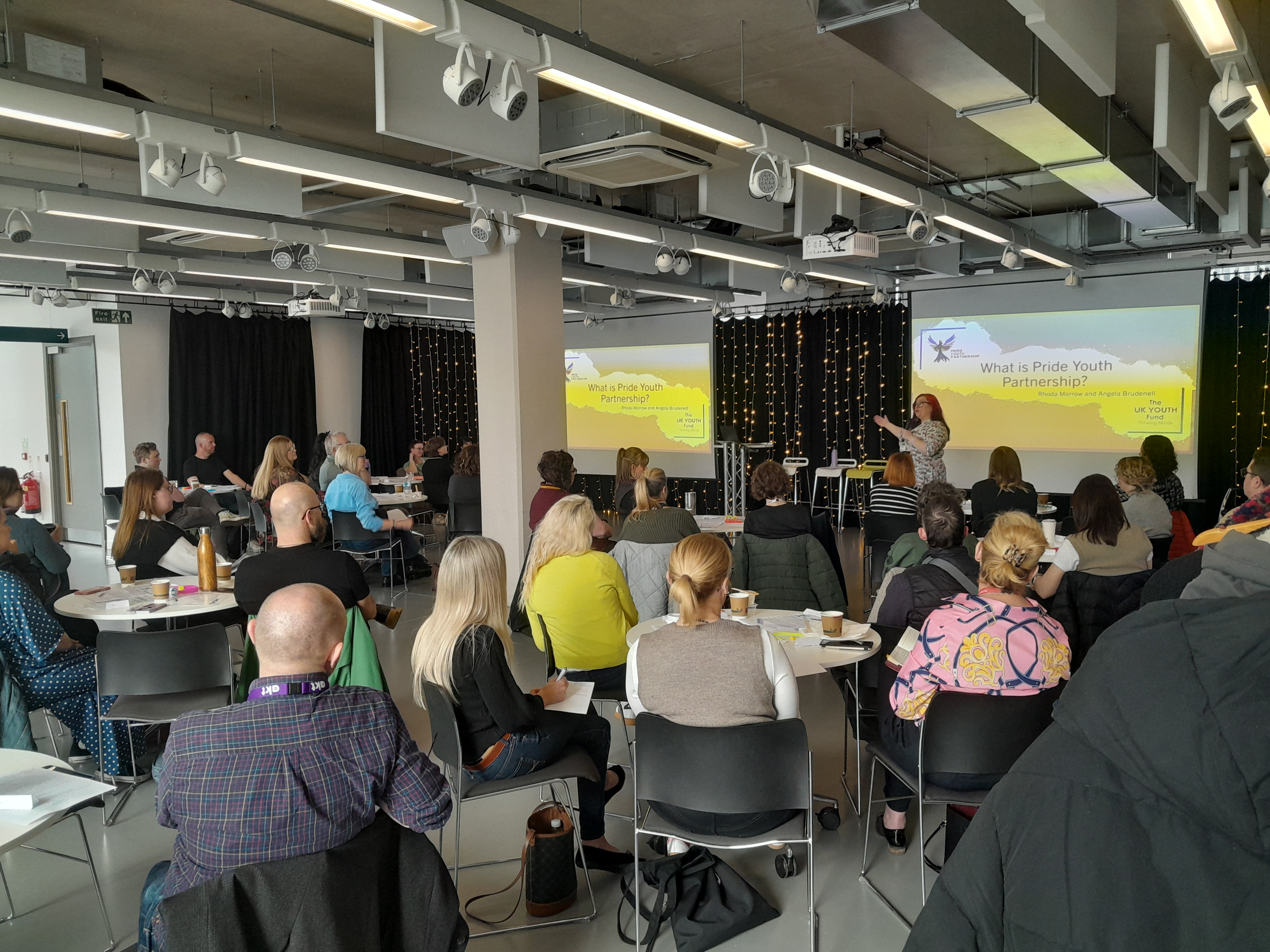 Room full of people listening to a presentation from the Pride Youth Partnership