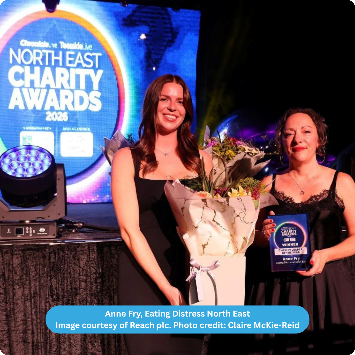 screen background stating North East Charity Awards 2026. In the foreground, 2 women holding a bunch of flowers and an award frame