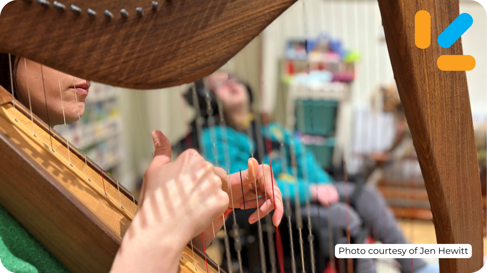 A photo of Jen playing the harp, her daughter is visible through the strings, her image is out of focus and she’s seated in a wheelchair listening to the music. Photo courtesy of Jen Hewitt.