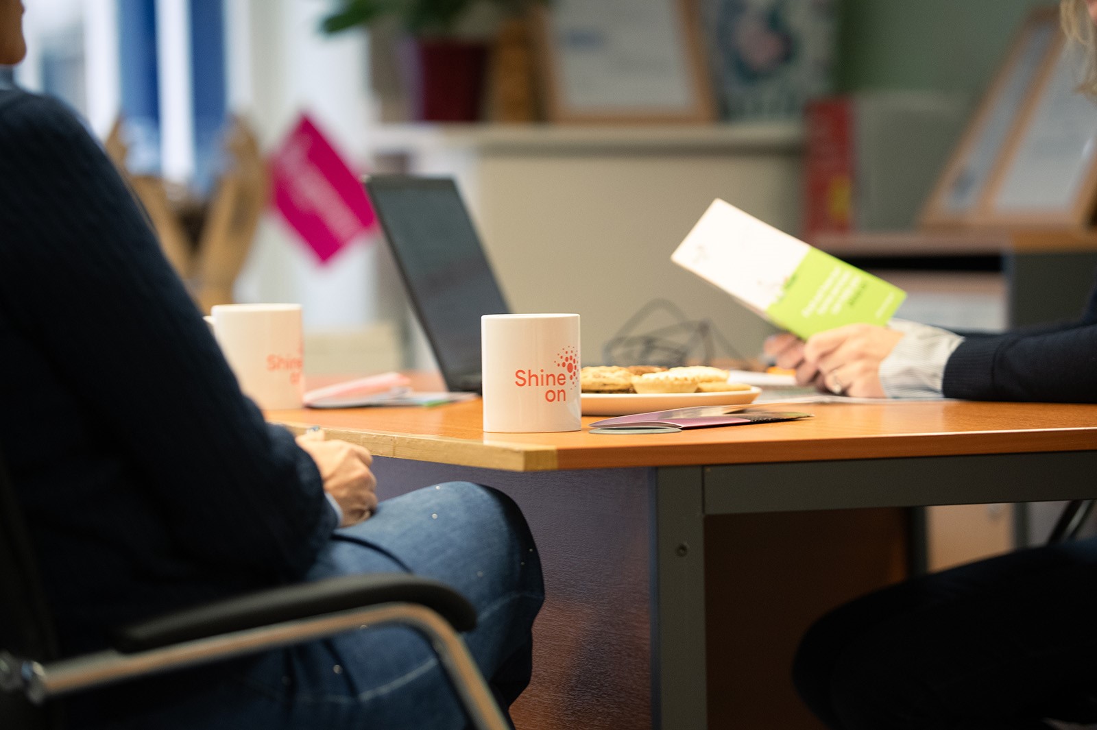 Photo of two people sitting at a desk discussing support over a cup of tea